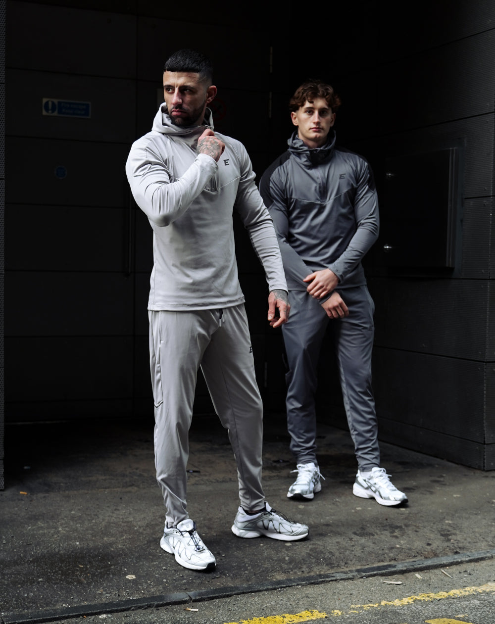 two men wearing light grey and dark grey tracksuit set on a road setting