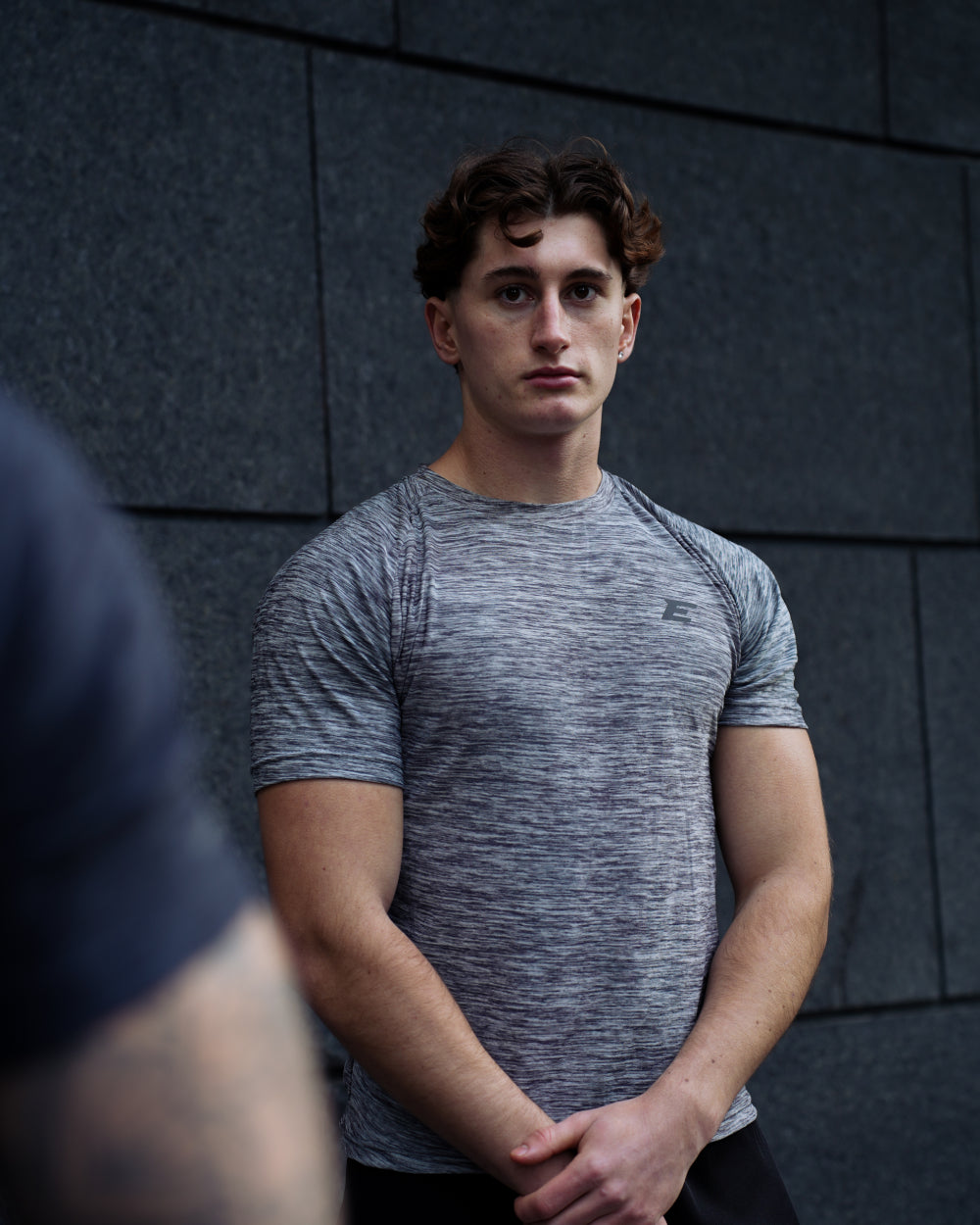 man wearing grey sportswear t-shirt on dark grey brick background