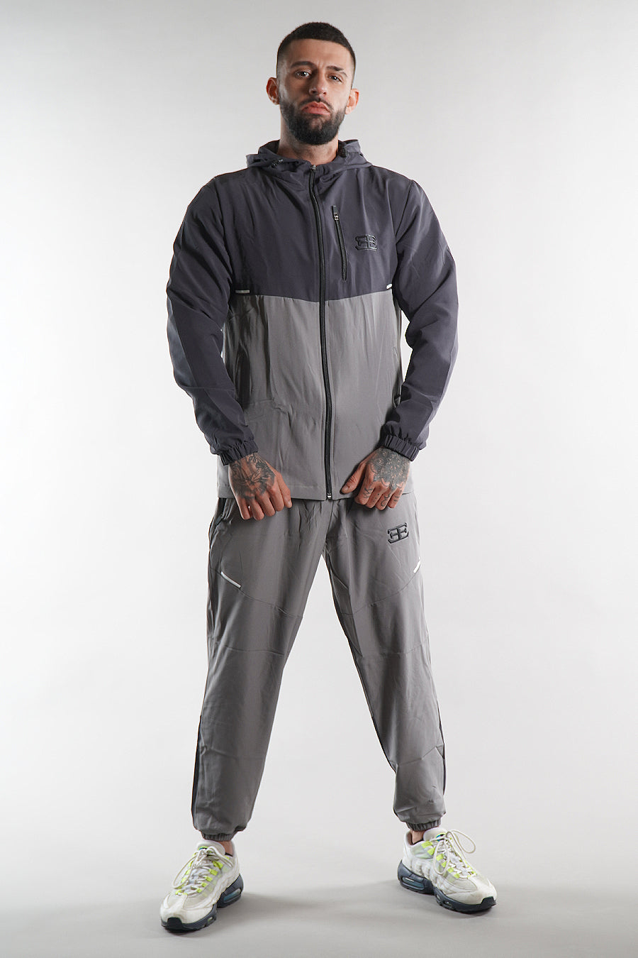 man wearing grey elegante logo tracksuit jacket and joggers on white background