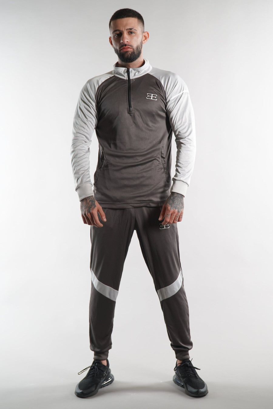 man wearing grey zip top and joggers tracksuit set, white background