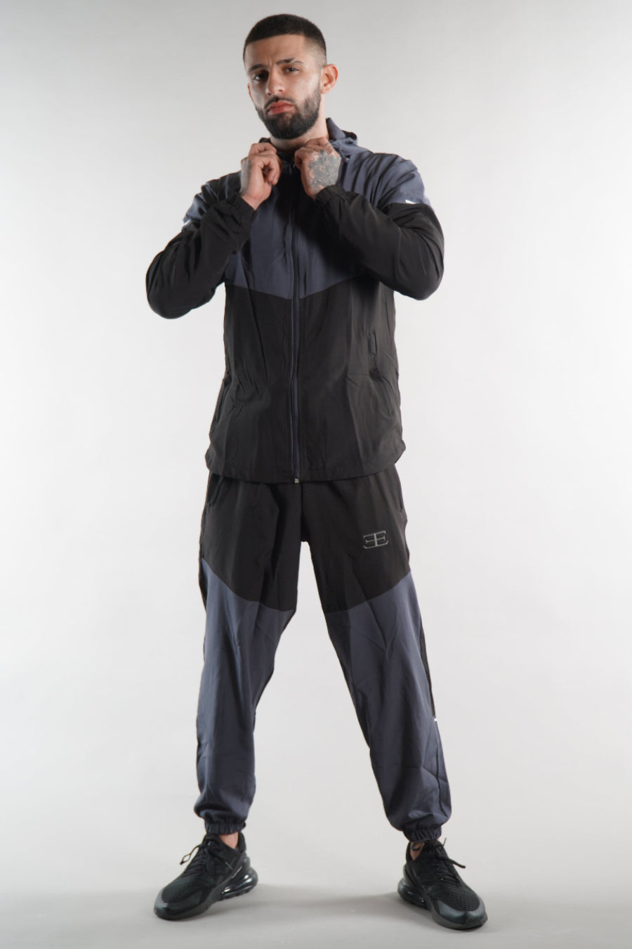 man wearing grey and black tracksuit jacket and joggers on white background