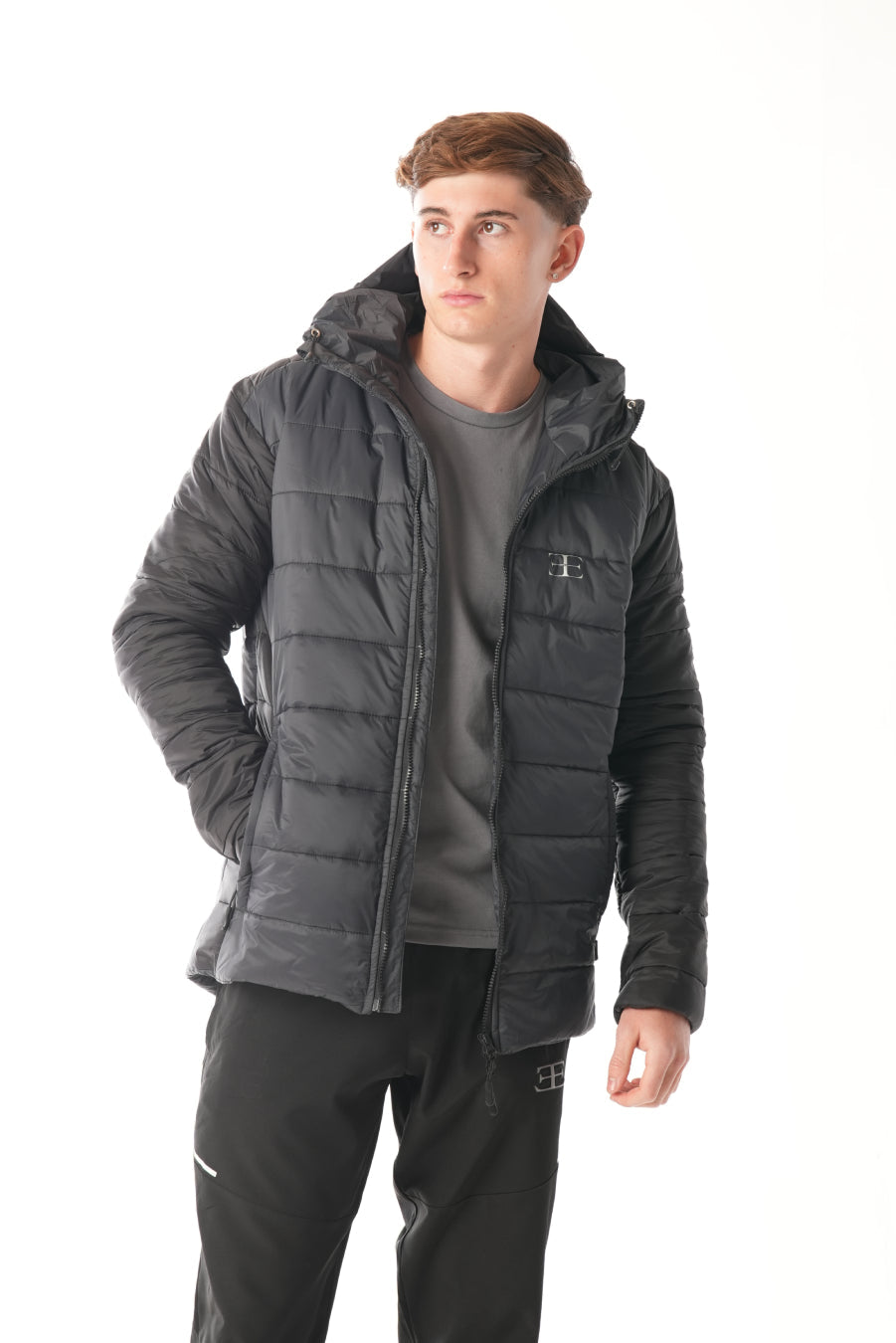 Man wearing a black puffer jacket over a gray t-shirt on a white background