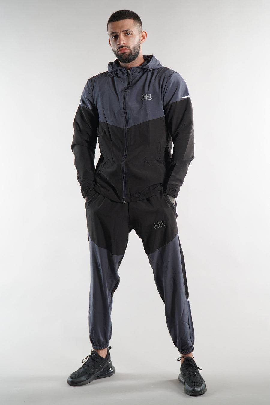 man wearing grey and black tracksuit jacket and joggers on a white background