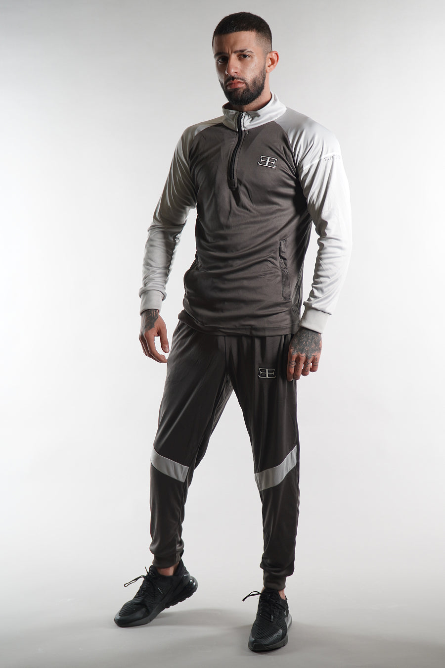 man wearing grey zip top and joggers tracksuit set, white background