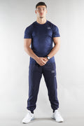 Man wearing a navy blue athletic outfit tshirt and joggers with a logo on a white background