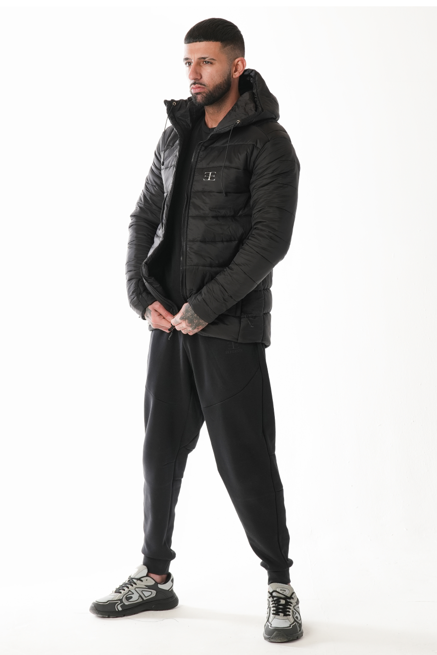 Man wearing a black puffer jacket and pants on a white background