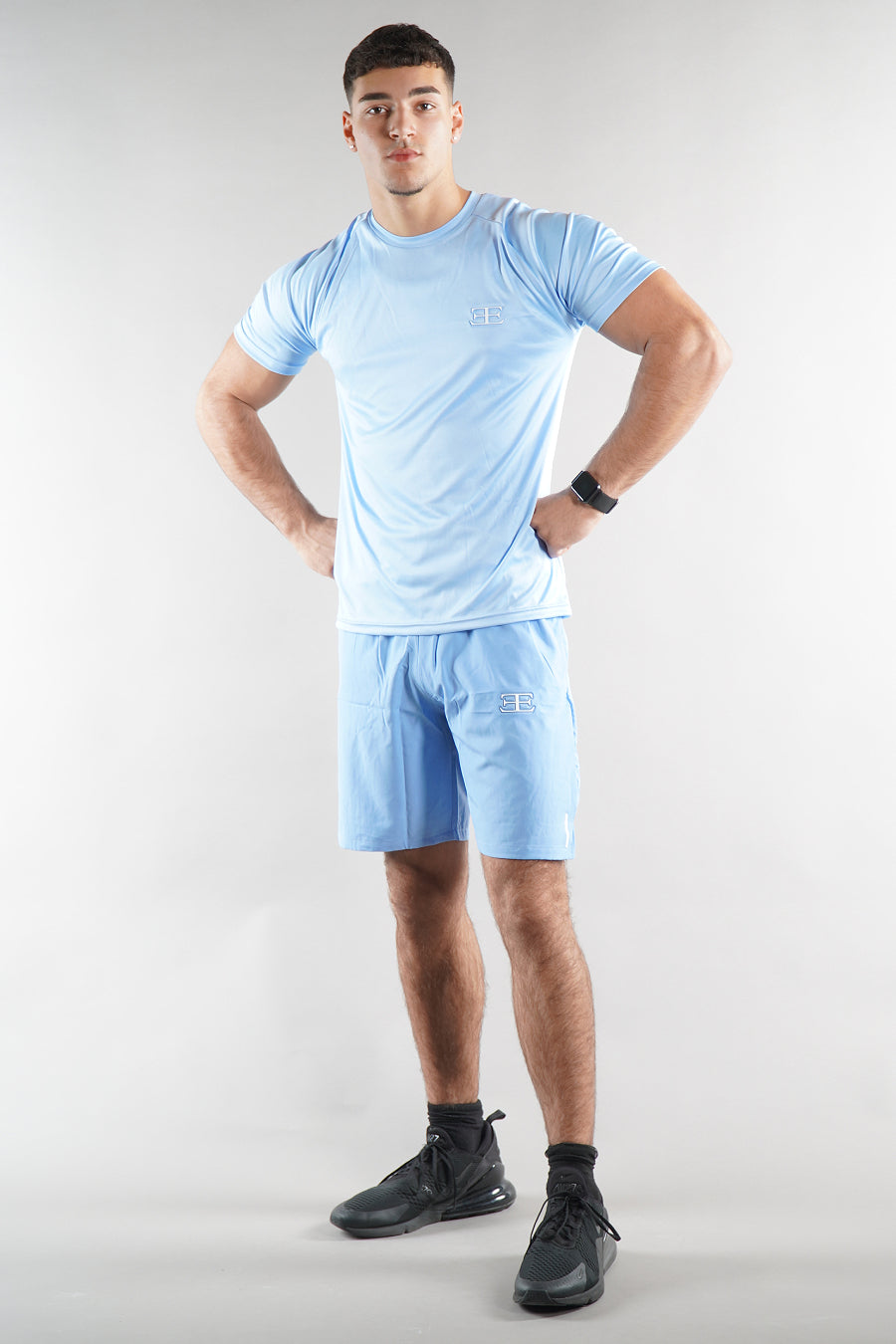 Man wearing a light blue athletic outfit with black shoes on a white background