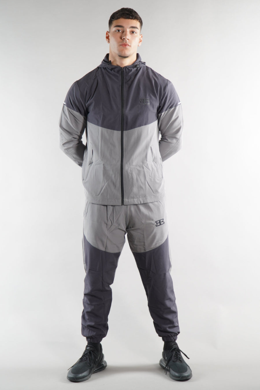 man wearing grey elegante logo tracksuit jacket and joggers on white background